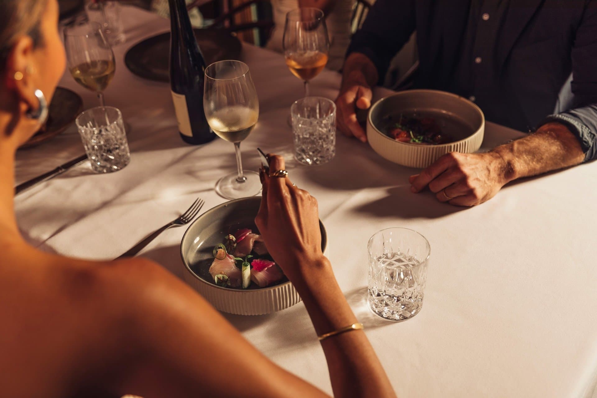 A group dining at a table with wine, crystal water glasses, and white linen tablecloth.