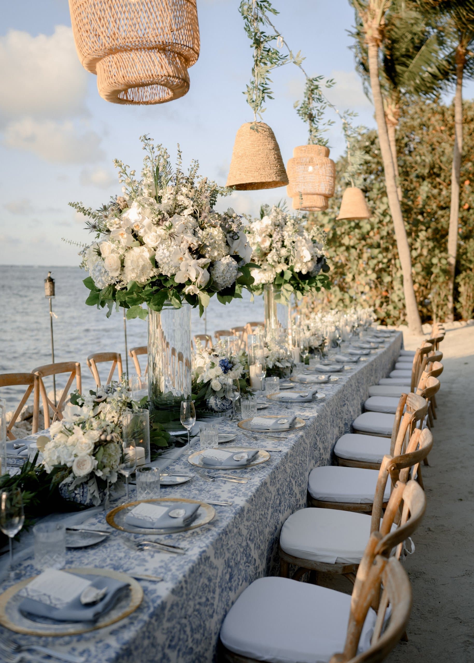 A dinner table set up on a white sand beach with the ocean in the background.