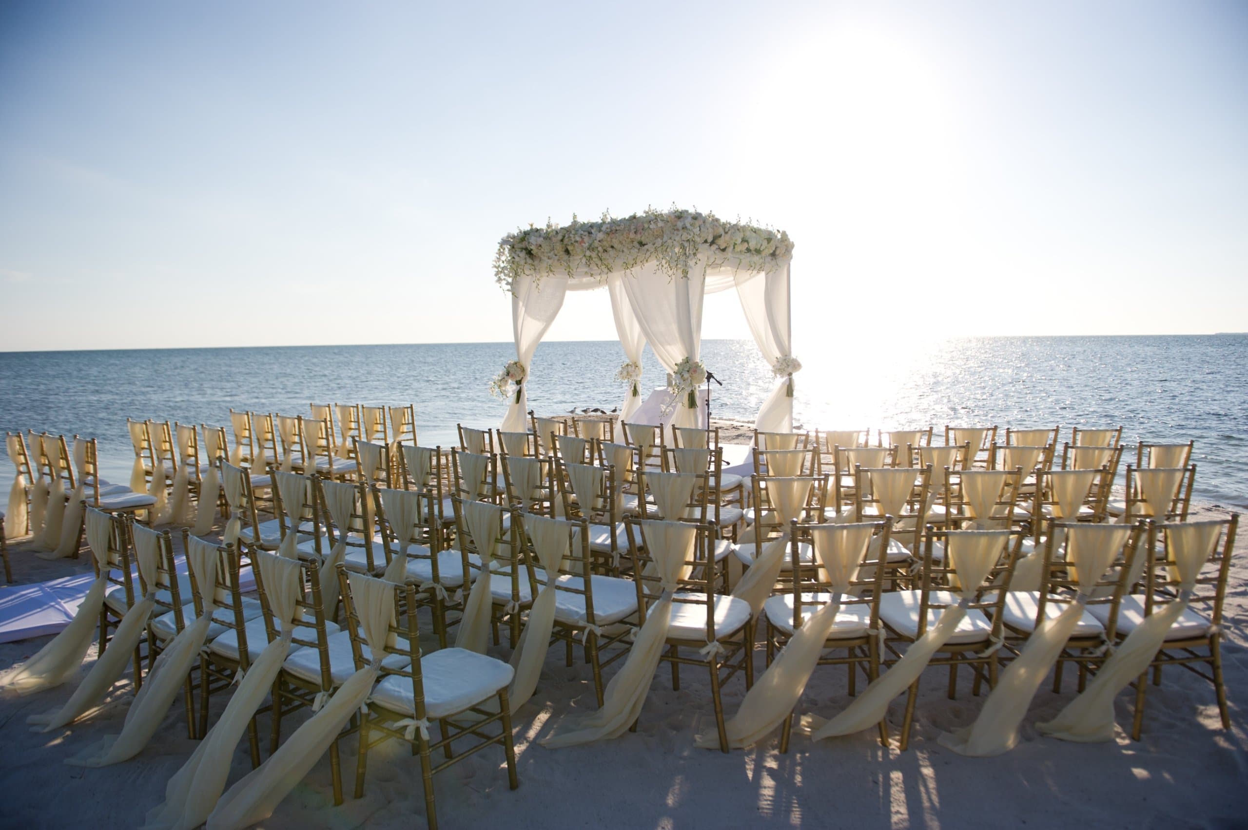 Chairs and a gazebo set up on a white sand beach for a wedding.