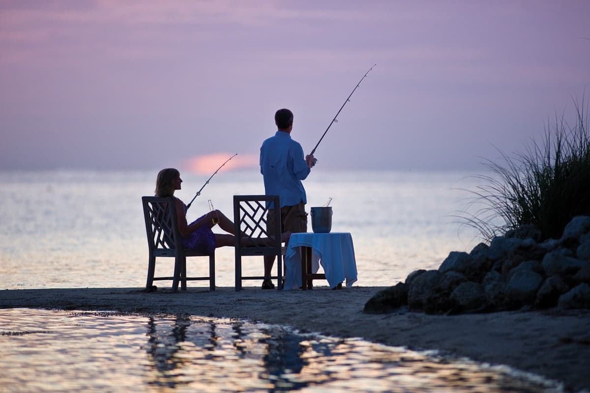 Man and woman fishing at sunset with a bucket of champagne beside them.