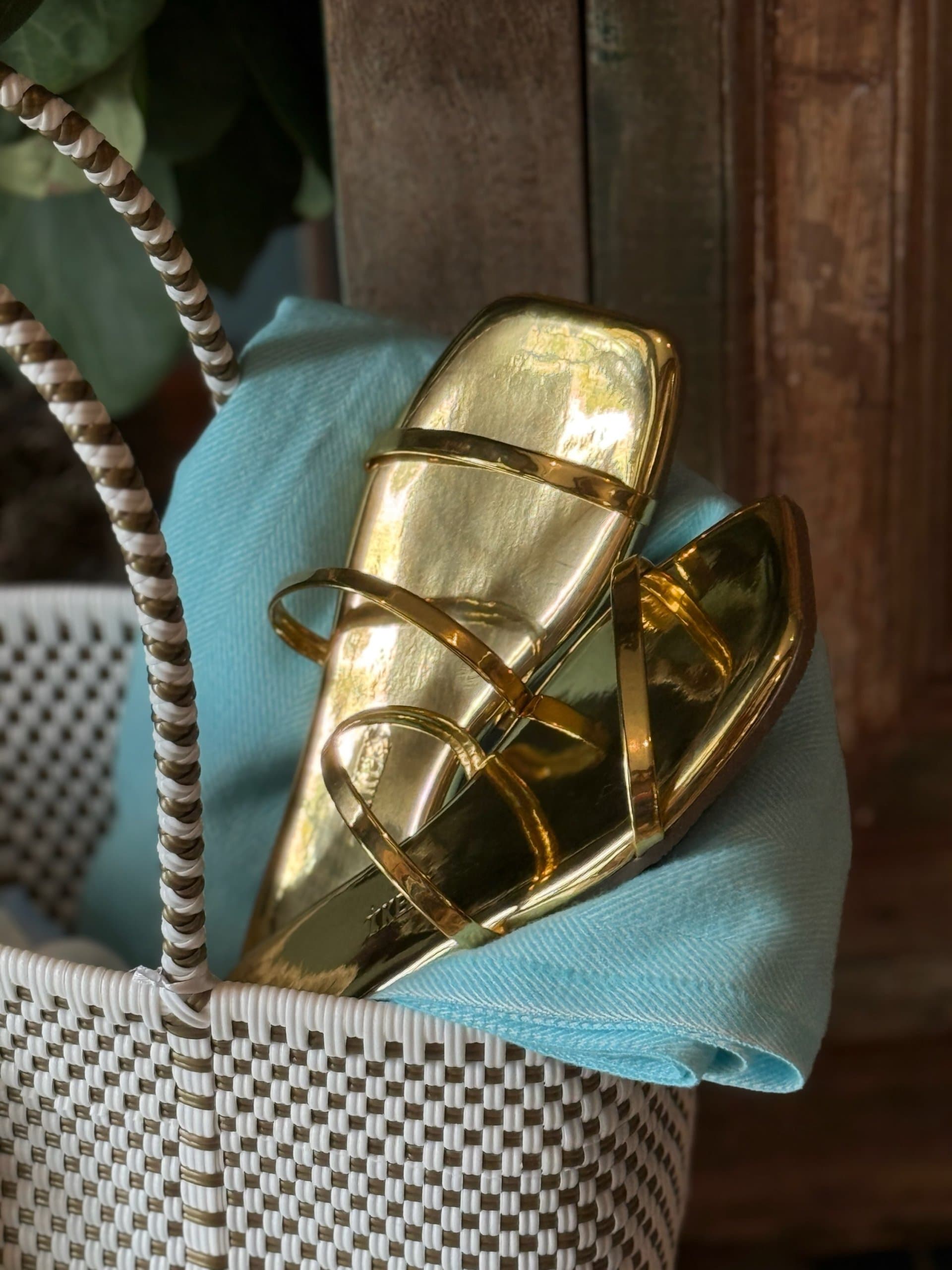 A pair of gold sandals sitting i a woven beach bag.