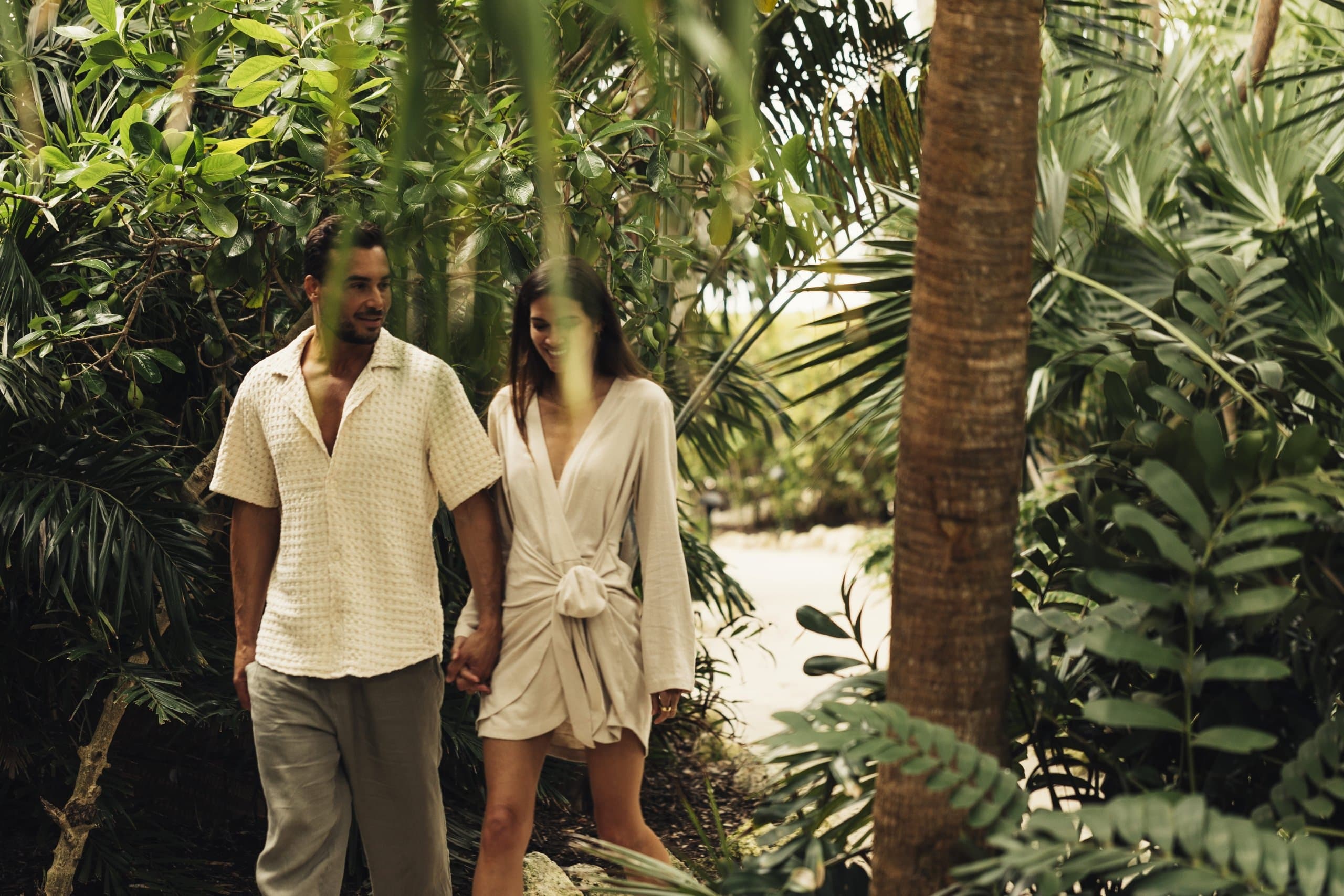 A couple walking hand in hand through a tropical forest.