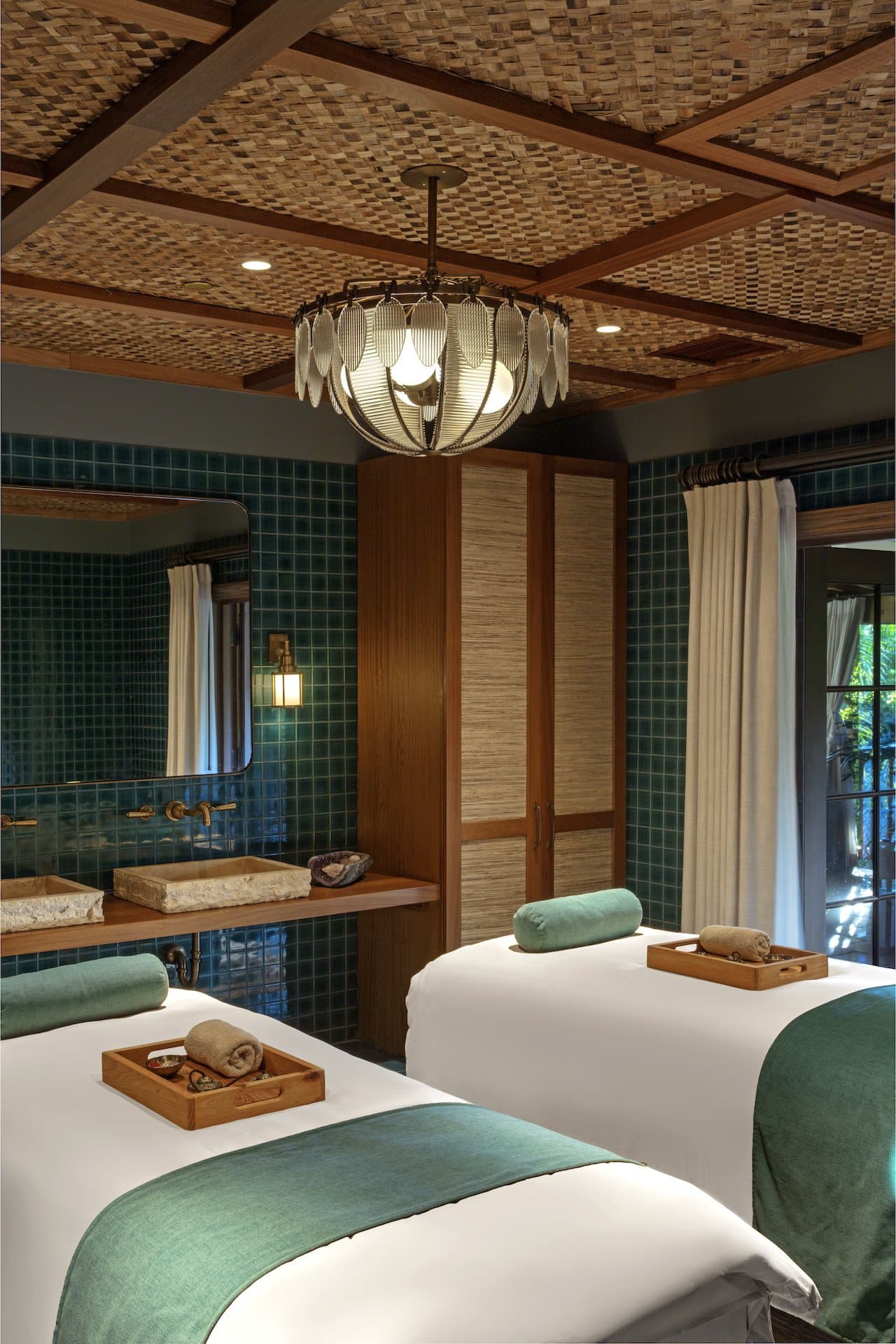A well lit spa with two massage tables with trays of towels and oil on top.