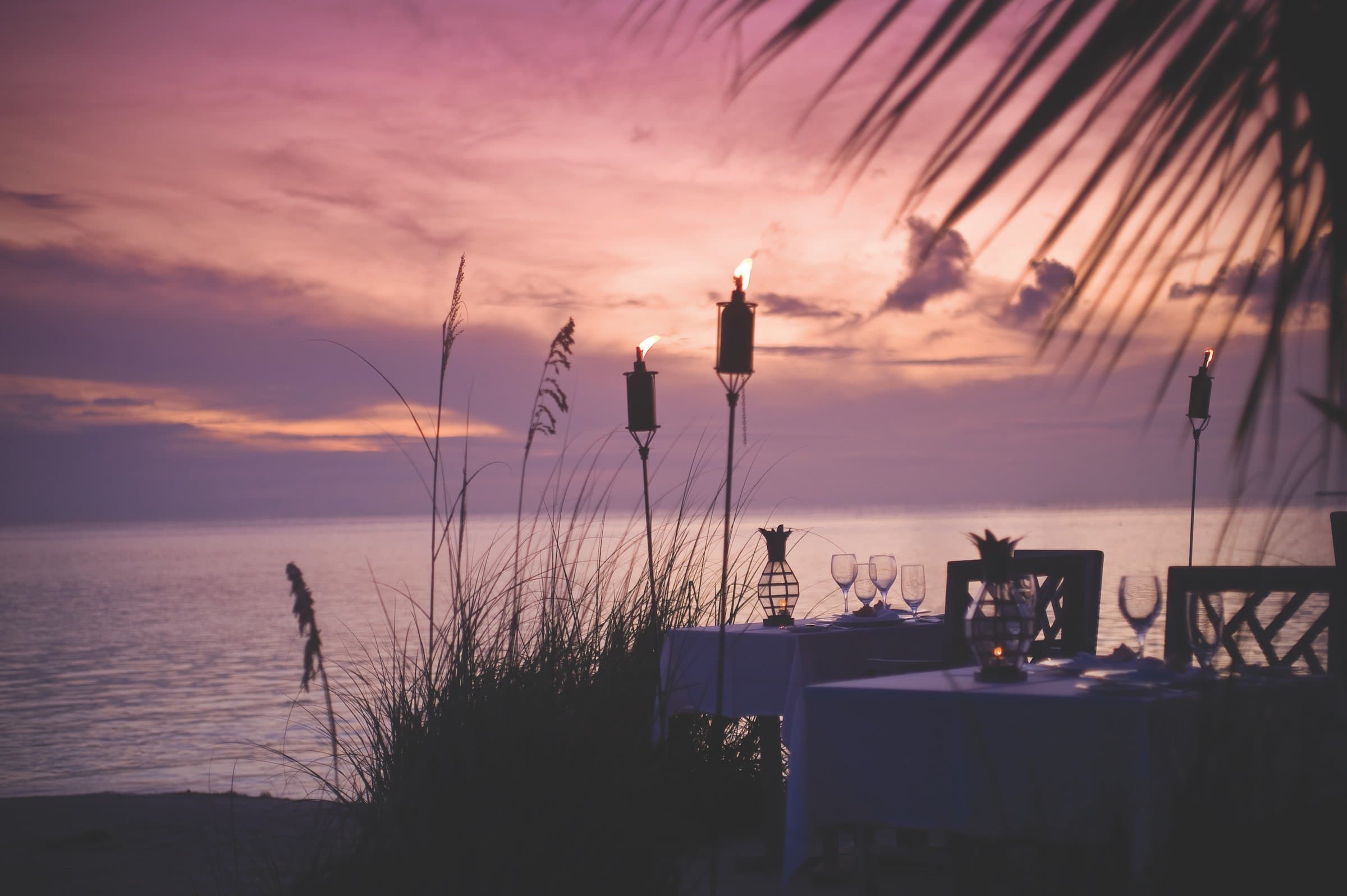Two tables set up for dinner at sunset along the water