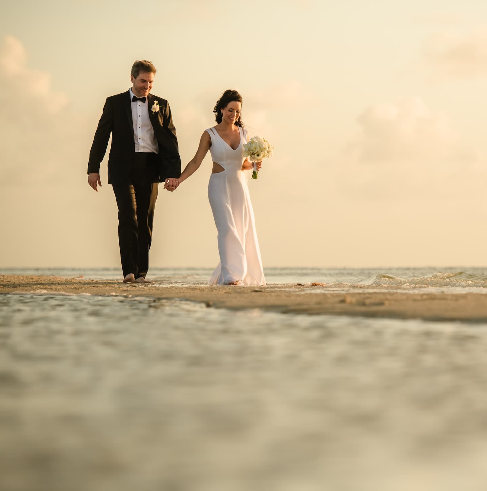 A bride and groom walking hand in hand along the ocean shoreline at Little Palm Island Resort
