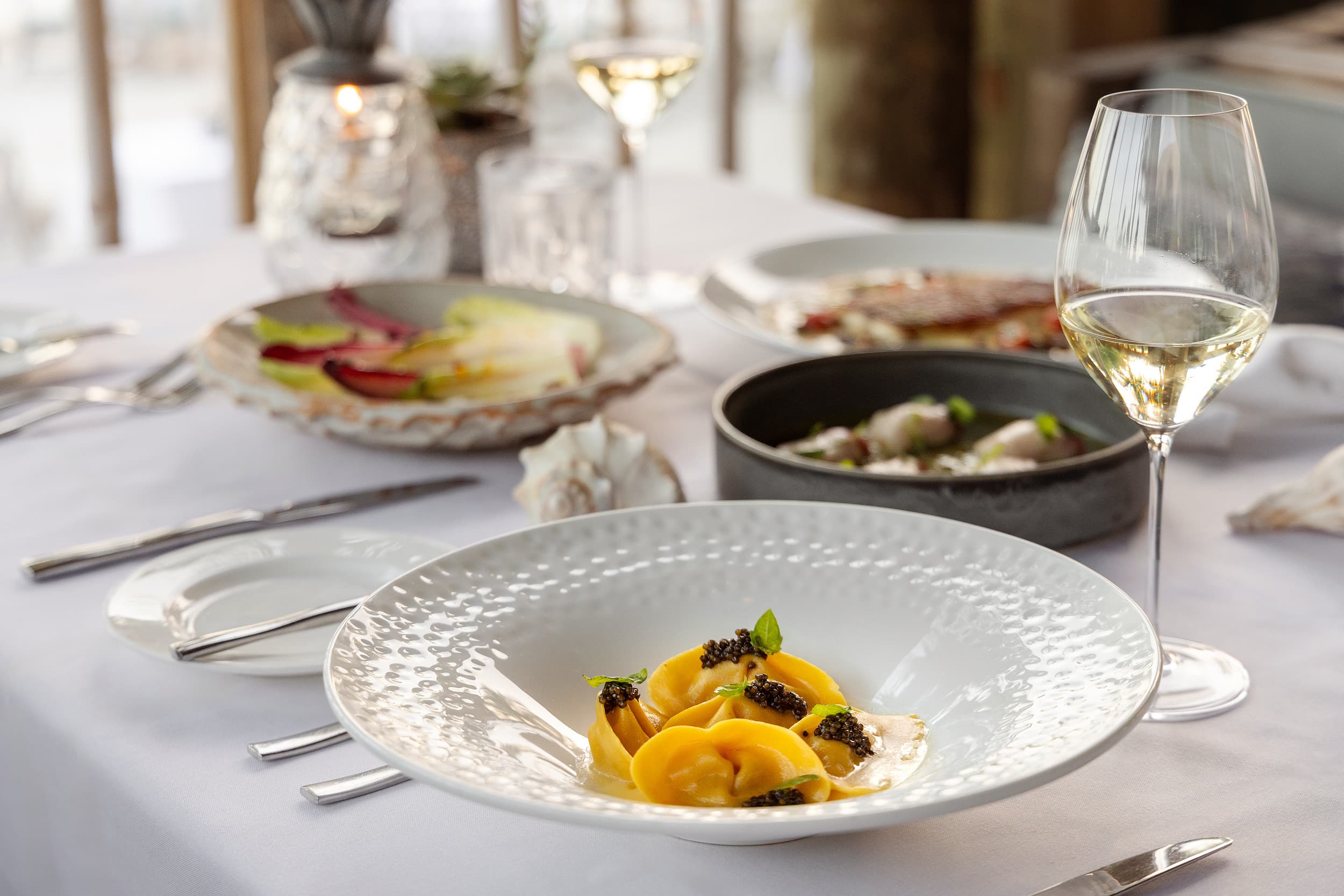 Handmade tortellini topped with caviar and basil in a textured white bowl, served with white wine at Little Palm Island Resort & Spa in the Florida Keys