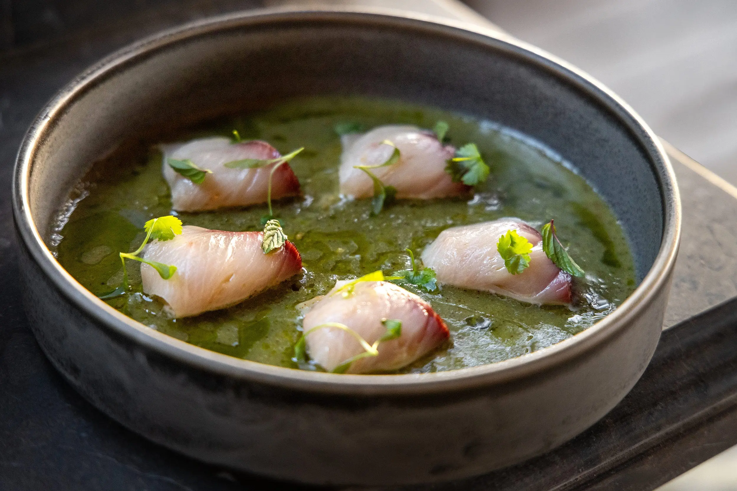 Raw fish crudo with fresh herbs in a green herb sauce, served in a dark stoneware bowl at a Florida Keys restaurant