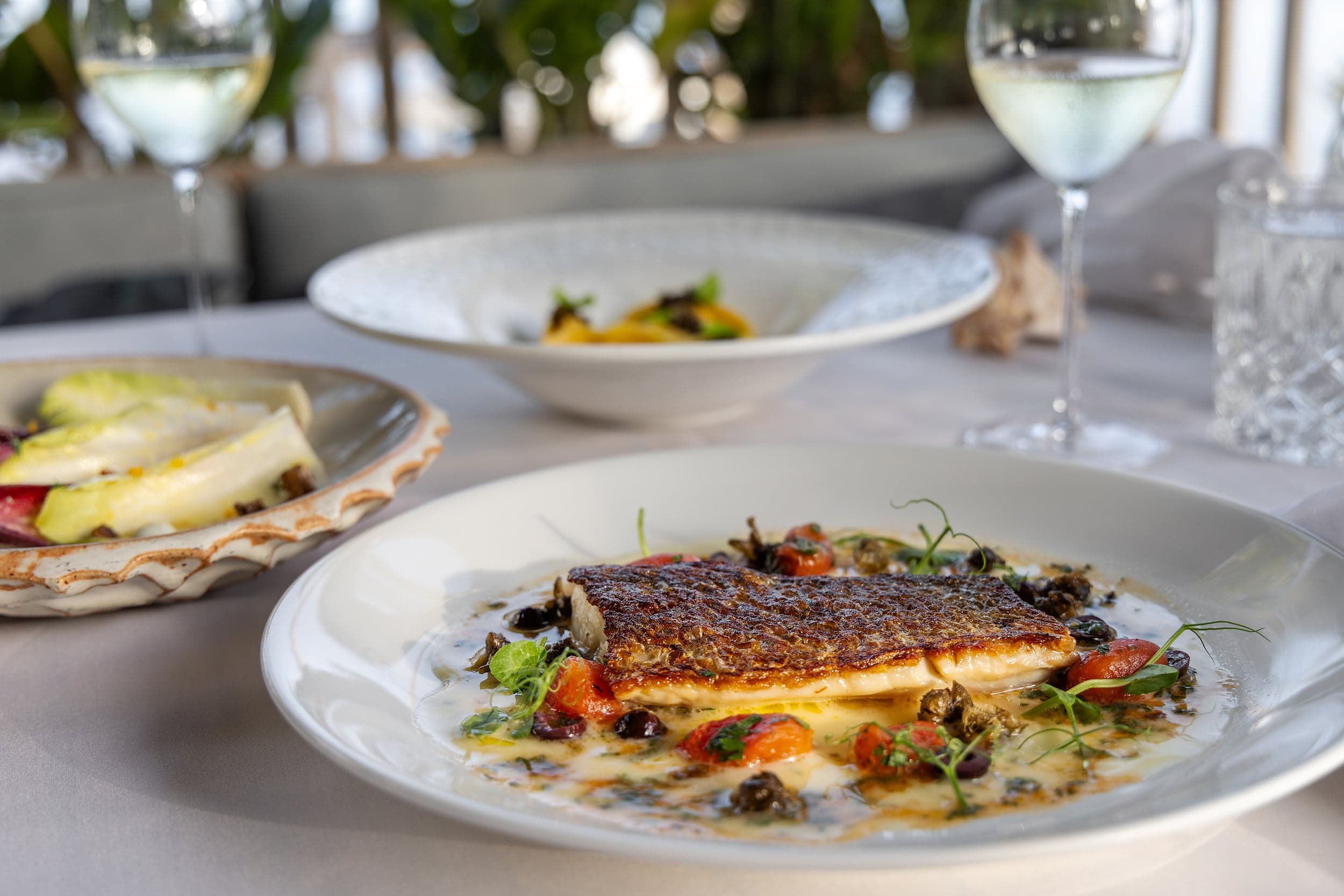 Seared fish entrée with cherry tomatoes and olives served alongside white wine and shared plates at a waterfront Florida Keys restaurant