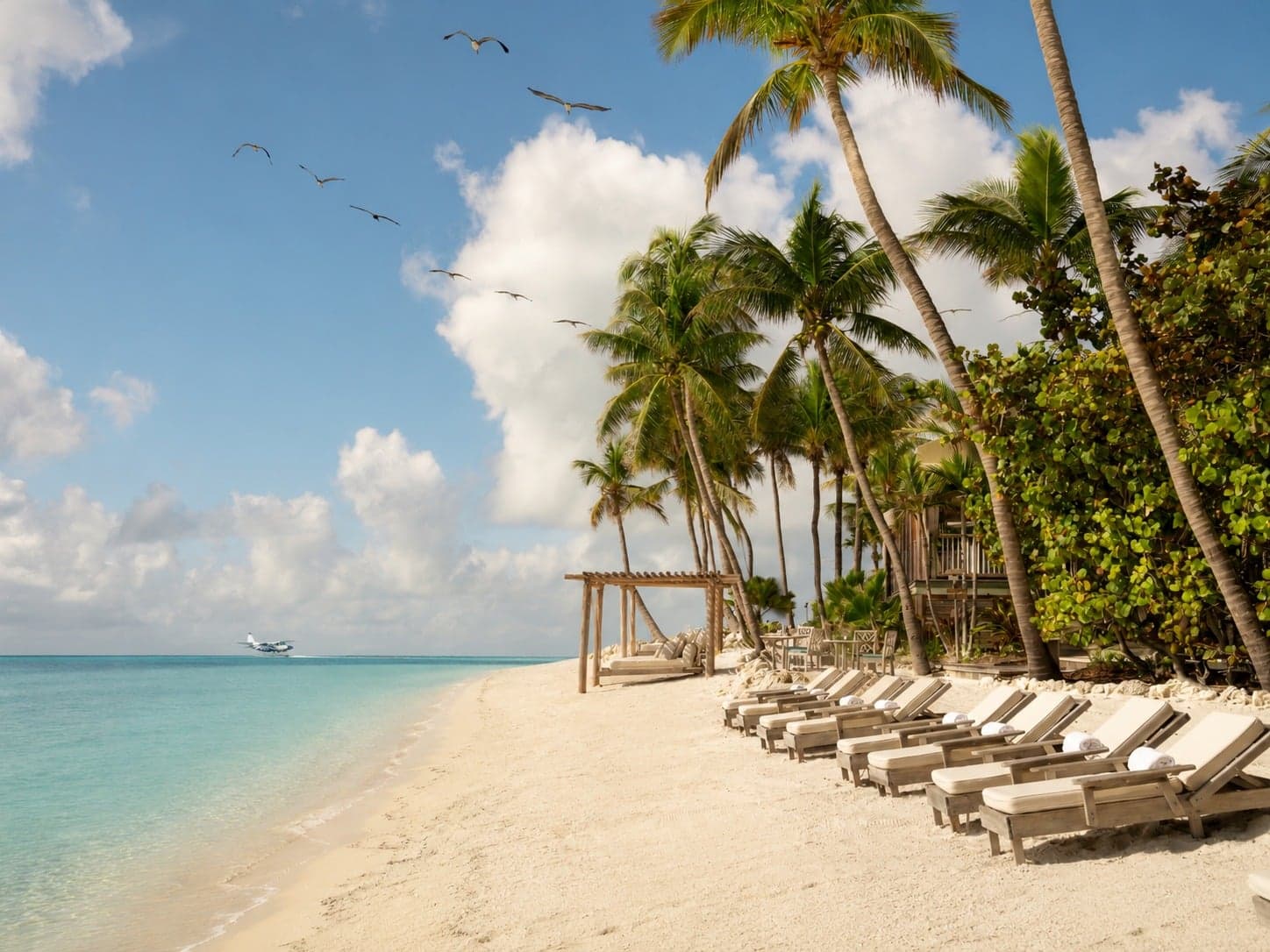 Seaplane landing offshore at Little Palm Island, a secluded private island resort in the Florida Keys, with palm trees and beach lounge chairs lining the white sand
