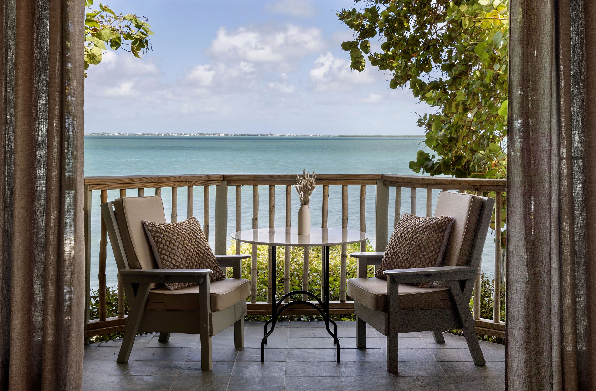 Private oceanfront balcony with woven pillows and bistro table overlooking turquoise water at Little Palm Island Resort & Spa in the Florida Keys.
