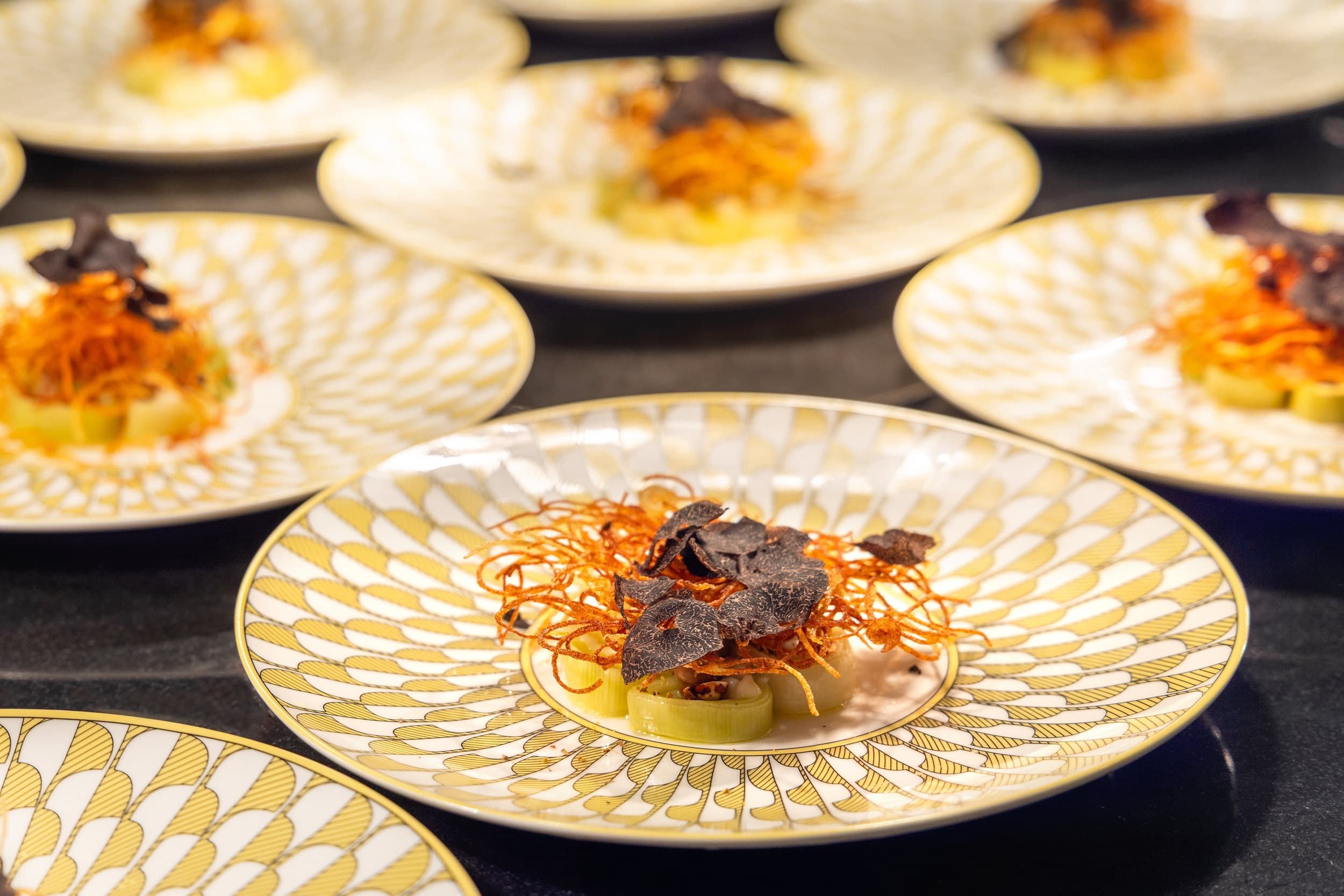Fine dining course of braised leeks with black truffle and crispy potato threads plated on gold porcelain at Little Palm Island Resort in the Florida Keys