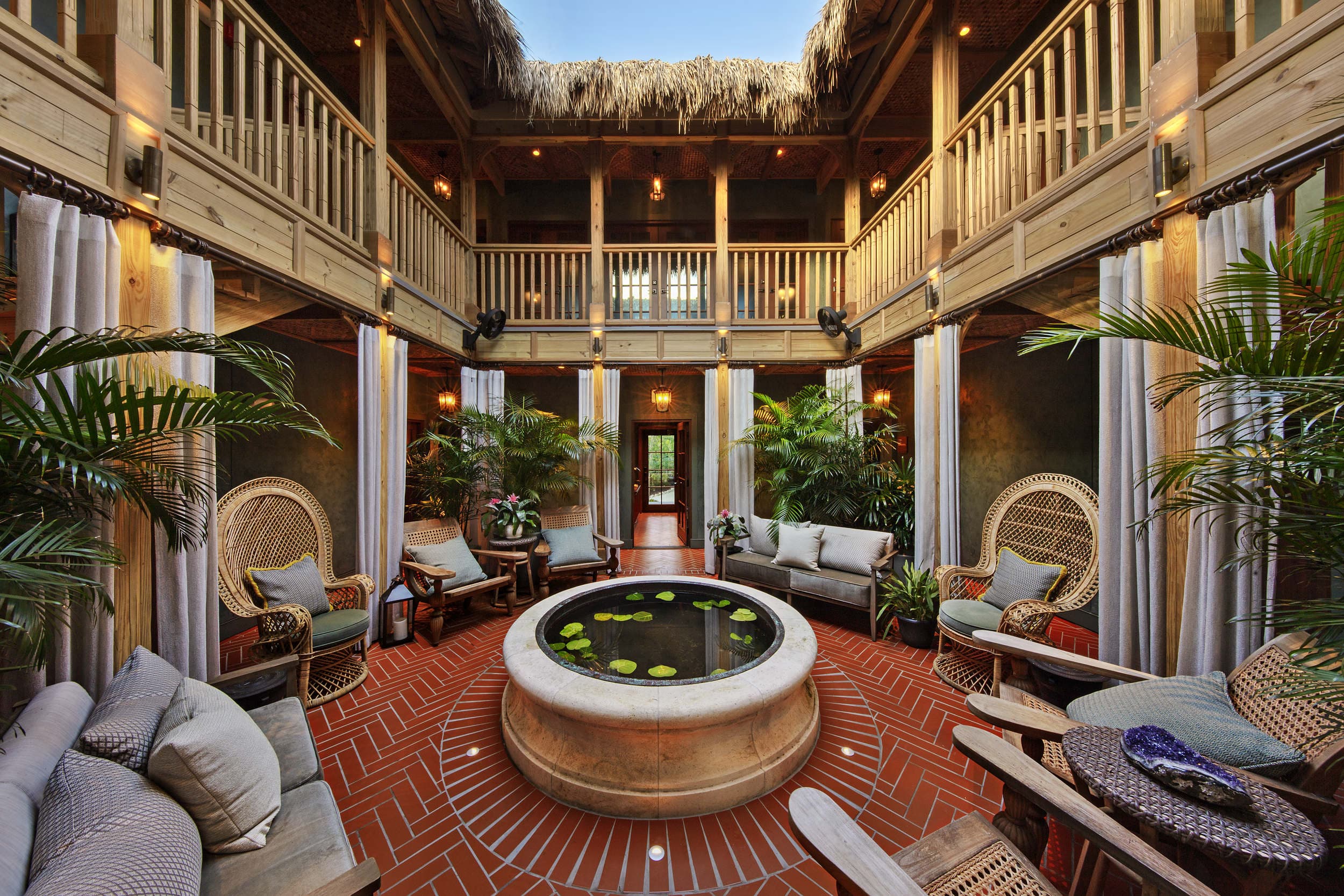 Tropical open-air courtyard with a round lily pond fountain, wicker seating, and wooden balconies surrounded by palms at Little Palm Island in Florida.